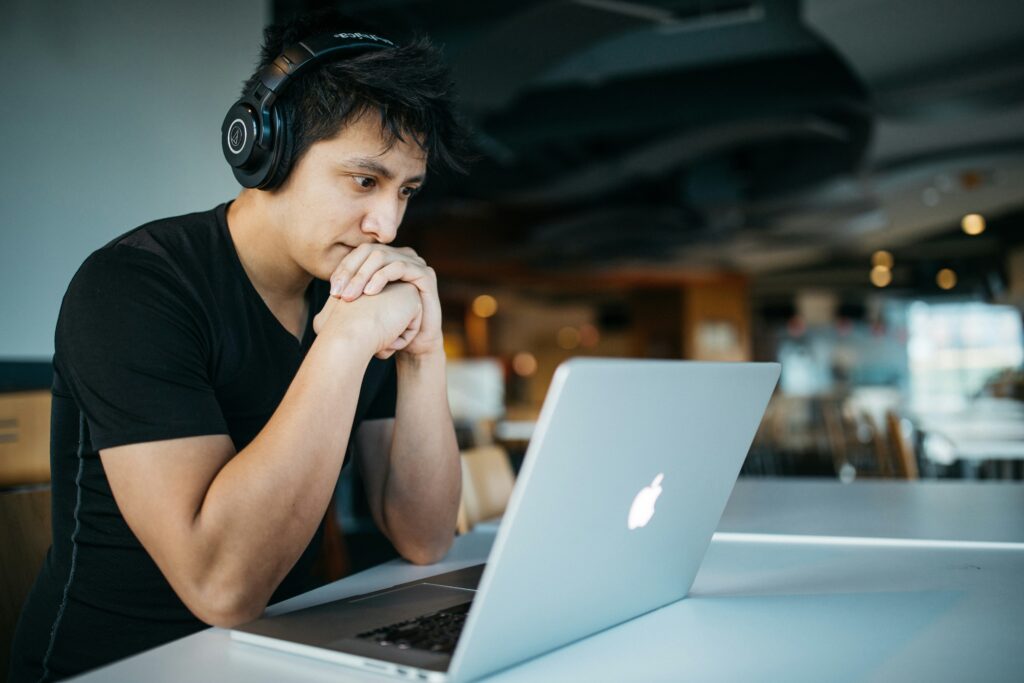 Man wearing headphones while sitting on chair in front of MacBook